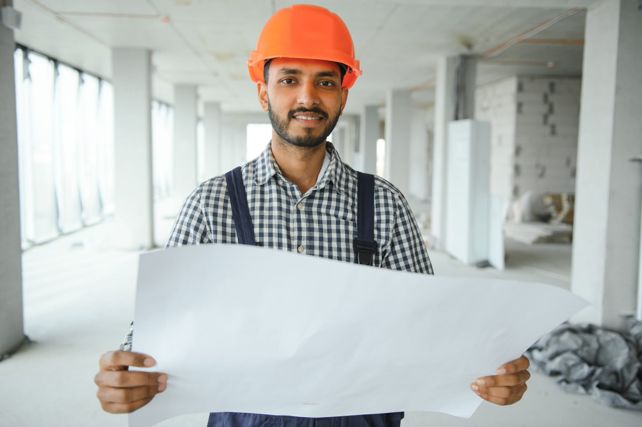 Indian construction site manager standing wearing helmet, thinking at construction site. Portrait of mixed race manual worker or architect